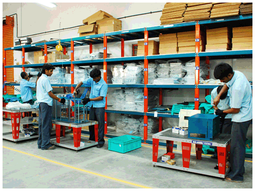 Operators working at assembly benches beside racked component shelving
